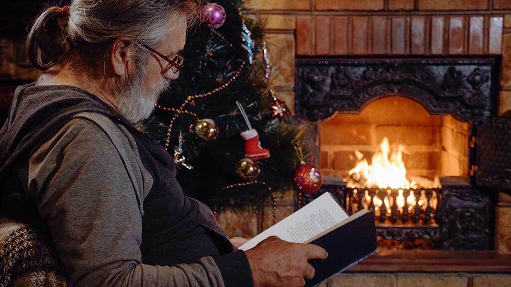 Senior man reading book near the fireplace and Christmas tree at xmas eve Senior man reading book near the fireplace and decorated Christmas tree at xmas eve, slow motion.