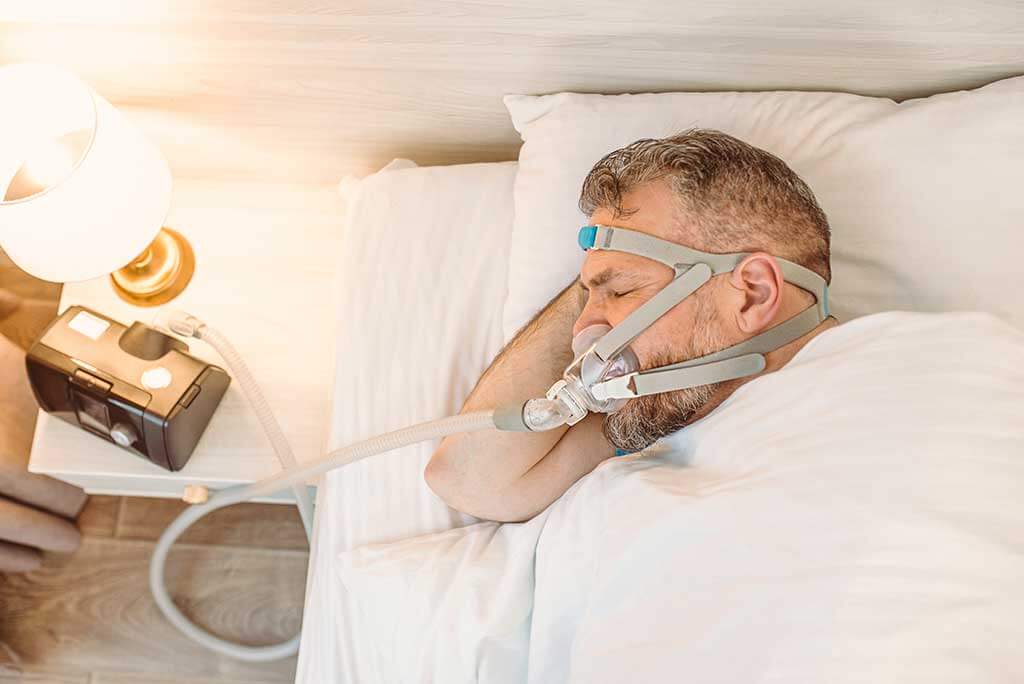Sleeping man with chronic breathing issues considers using CPAP Sleeping man with chronic breathing issues considers using CPAP machine in bed