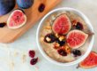 Autumn oatmeal with red figs, cranberries and walnuts in a bowl, overhead scene on white marble