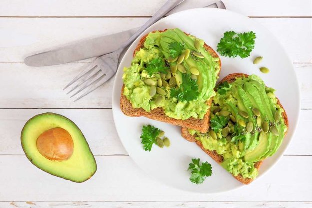 Avocado toasts with pumpkin and chia seeds on whole grain bread. Avocado toasts with pumpkin and chia seeds on whole grain bread. Above view on a white wood background.