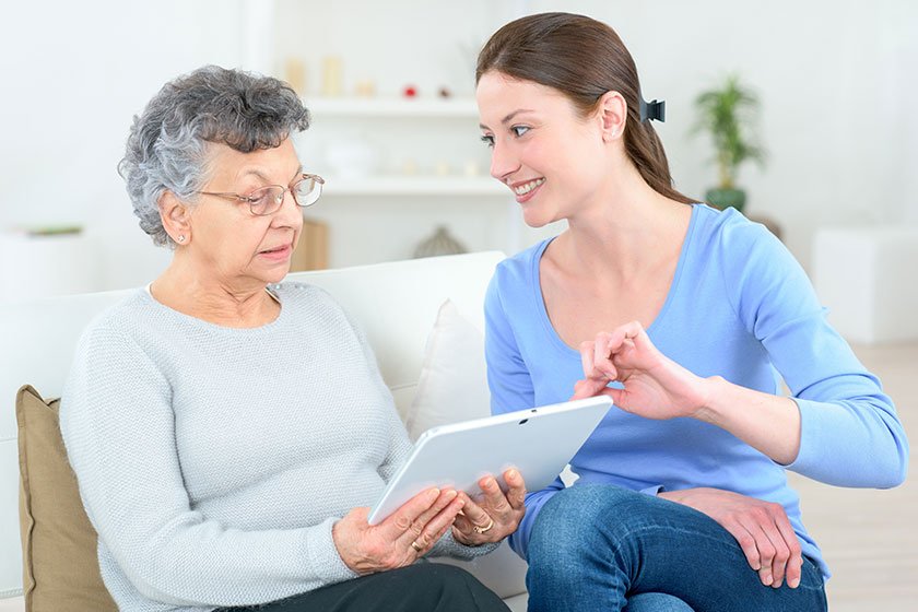 young lady helping elderly woman use a digital tablet