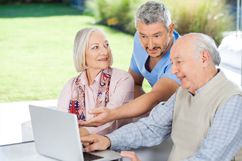Male Caretaker Showing Something To Senior Couple On Laptop Male Caretaker Showing Something To Senior Couple On Laptop