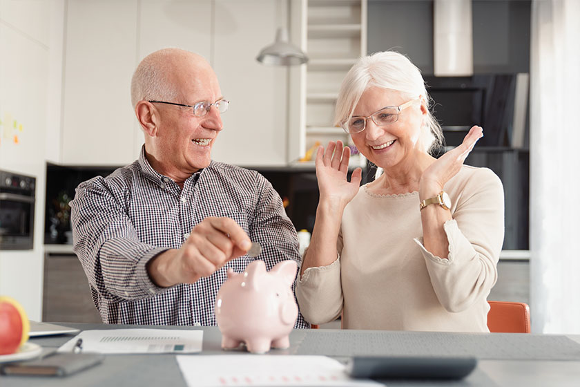 Senior couple putting coin into piggy bank Senior couple putting coin into piggy bank