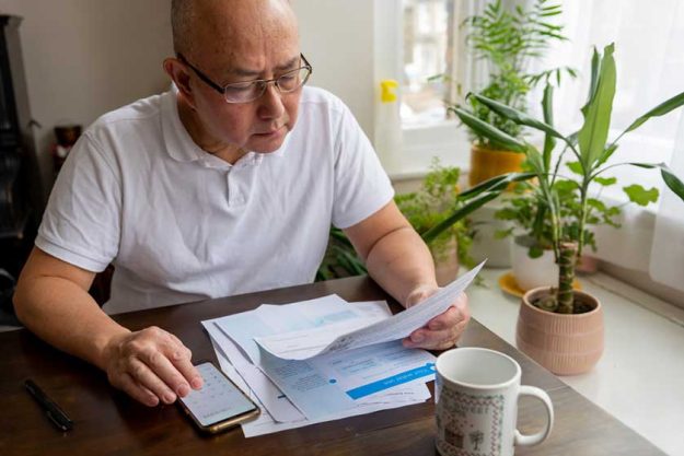 A senior man sitting by a table calculating A senior man sitting by a table calculating