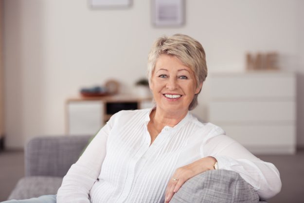 Smiling Senior Woman Sitting at the Gray Couch How A Senior Living Facility In Tulsa, OK Gives Residents Privacy