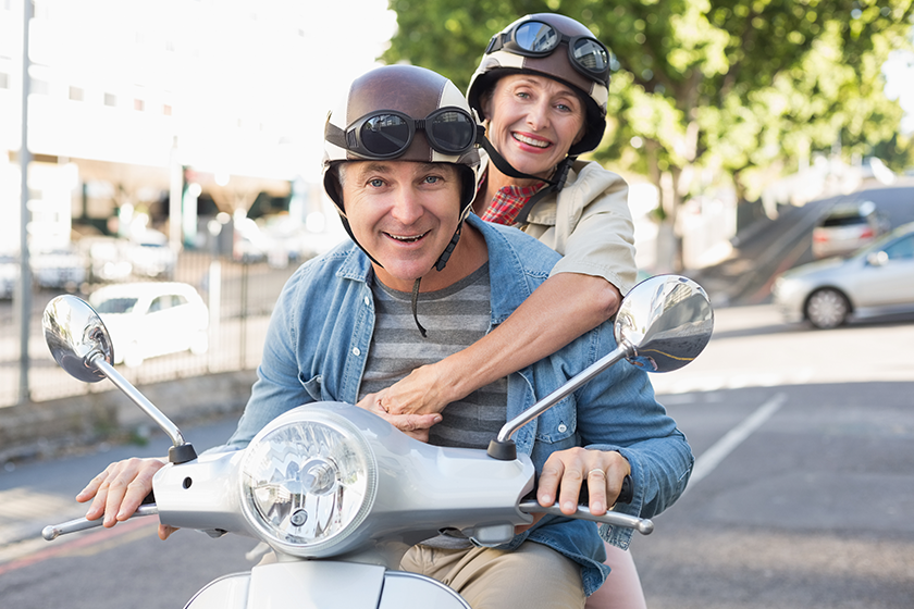 Happy mature couple riding a scooter in the city