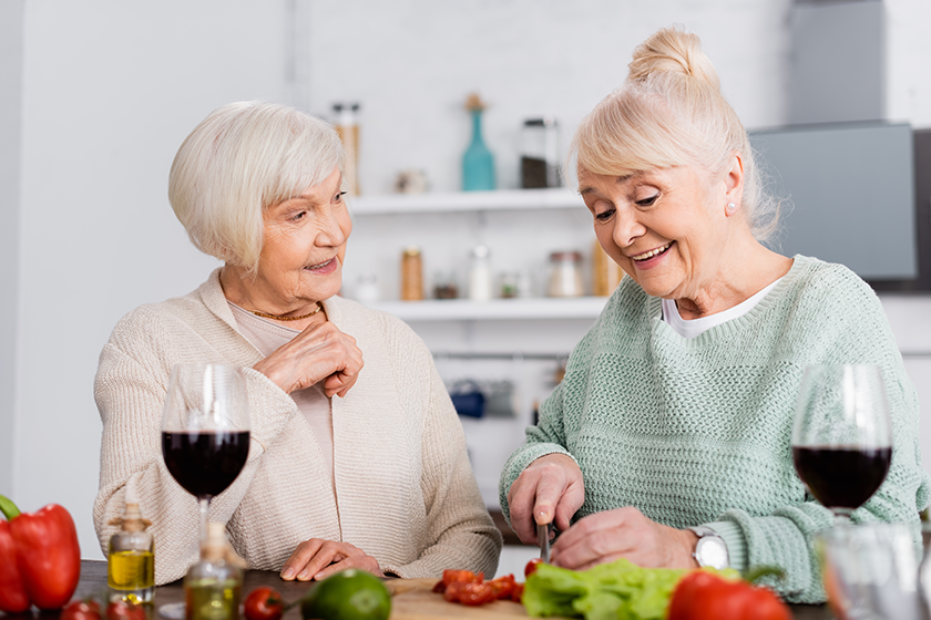 Happy senior woman looking at joyful friend cutting vegetables Happy senior woman looking at joyful friend cutting vegetables
