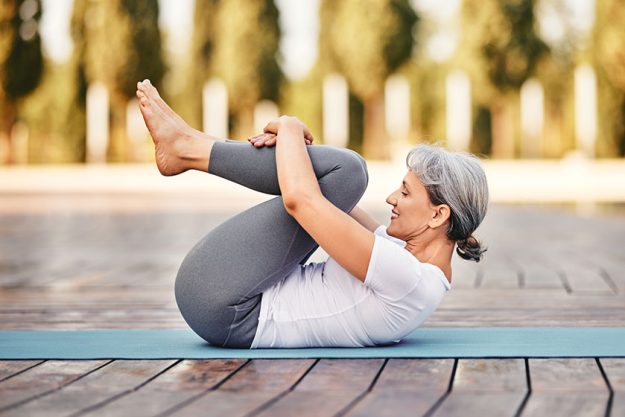 Side view of mature woman in sports wear lying on mat hugging her Side view of mature woman in sports wear lying on mat hugging her