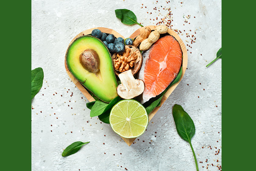 Foods good for the heart: nuts, salmon, avocados, spinach, mushrooms, berries. In a heart-shaped box. On a stone background. Top view.