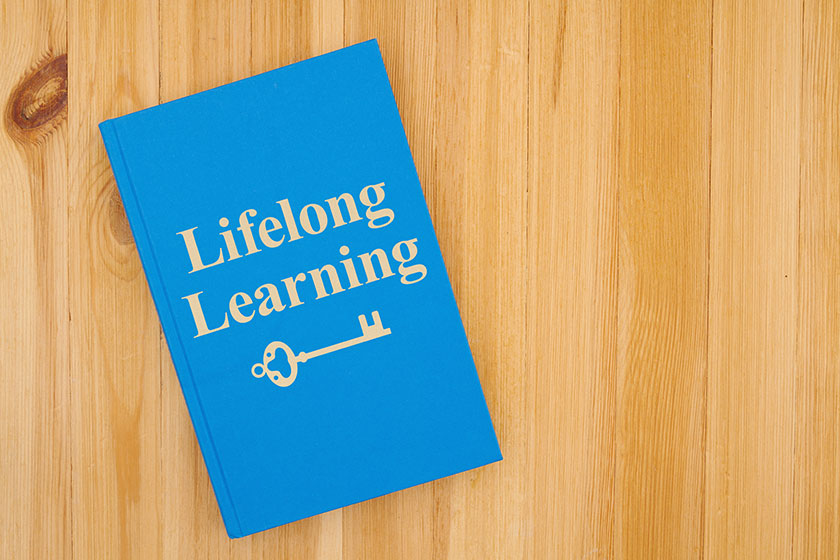 Lifelong learning message with a skeleton key icon written on a book on a wood desk Lifelong learning message with a skeleton key icon written on a book on a wood desk