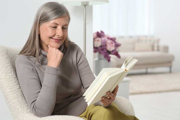 Beautiful-senior-woman-reading-book-armchair-home