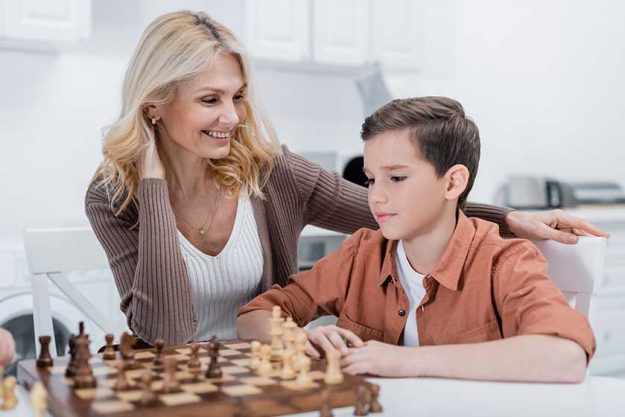 Middle-aged-woman-smiling-grandson-playing-chess-kitchen Middle-aged-woman-smiling-grandson-playing-chess-kitchen