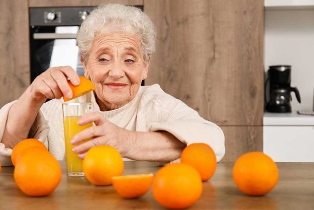 Senior-woman-squeezing-orange-juice-glass-kitchen- Senior-woman-squeezing-orange-juice-glass-kitchen-