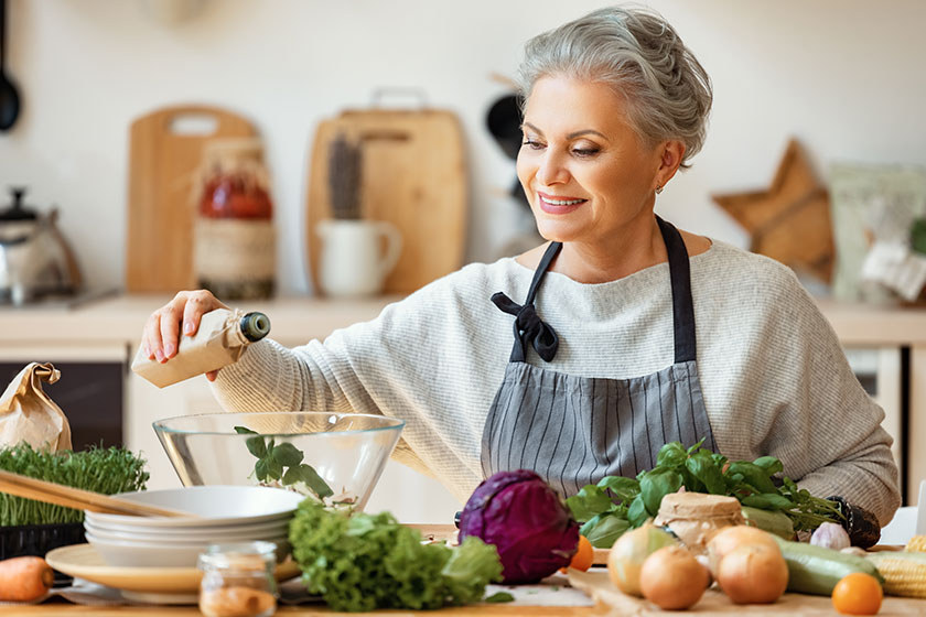 Cheerful middle aged housewife in apron pours Cheerful middle aged housewife in apron pours