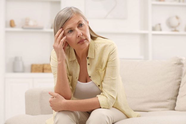 Menopause. Woman suffering from headache on sofa