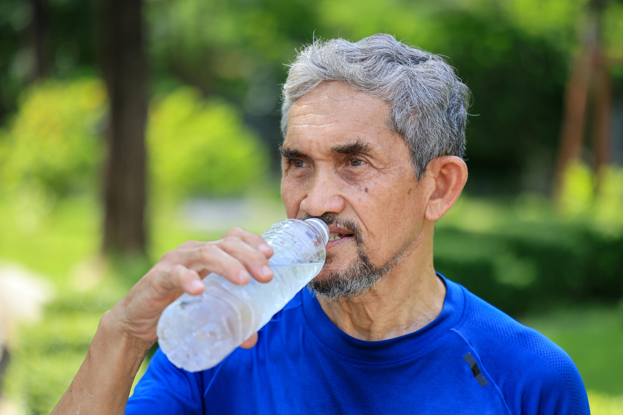 Senior Asian man is drinking water after morning exercise in the