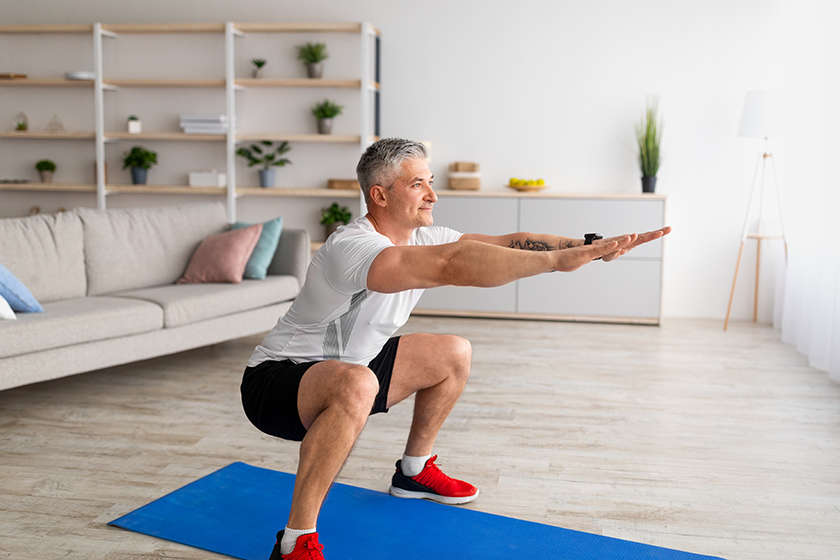 stay-home-alone-to-workout-fit-mature-man-in-sportswear-doing-squats Stay home alone to workout. Fit mature man